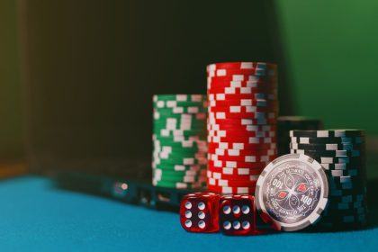 Fichas e dados de cassino ao lado de um laptop sobre uma mesa de feltro, representando apostas online.