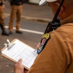 Policial registra informações em uma prancheta durante uma atividade de segurança ao ar livre.