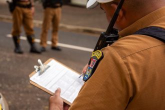 Policial registra informações em uma prancheta durante uma atividade de segurança ao ar livre.