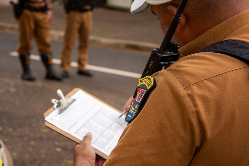 Policial registra informações em uma prancheta durante uma atividade de segurança ao ar livre.