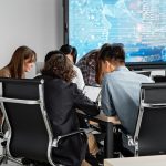 Equipe diversa reunida em um escritório moderno, colaborando diante de uma tela digital.