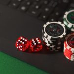 Fichas de cassino e dados sobre uma superfície escura, em referência a apostas e jogos de azar online.